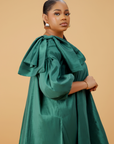 Model wearing an emerald green satin bow sleeve dress with voluminous sleeves and structured bow detail on the shoulder.
