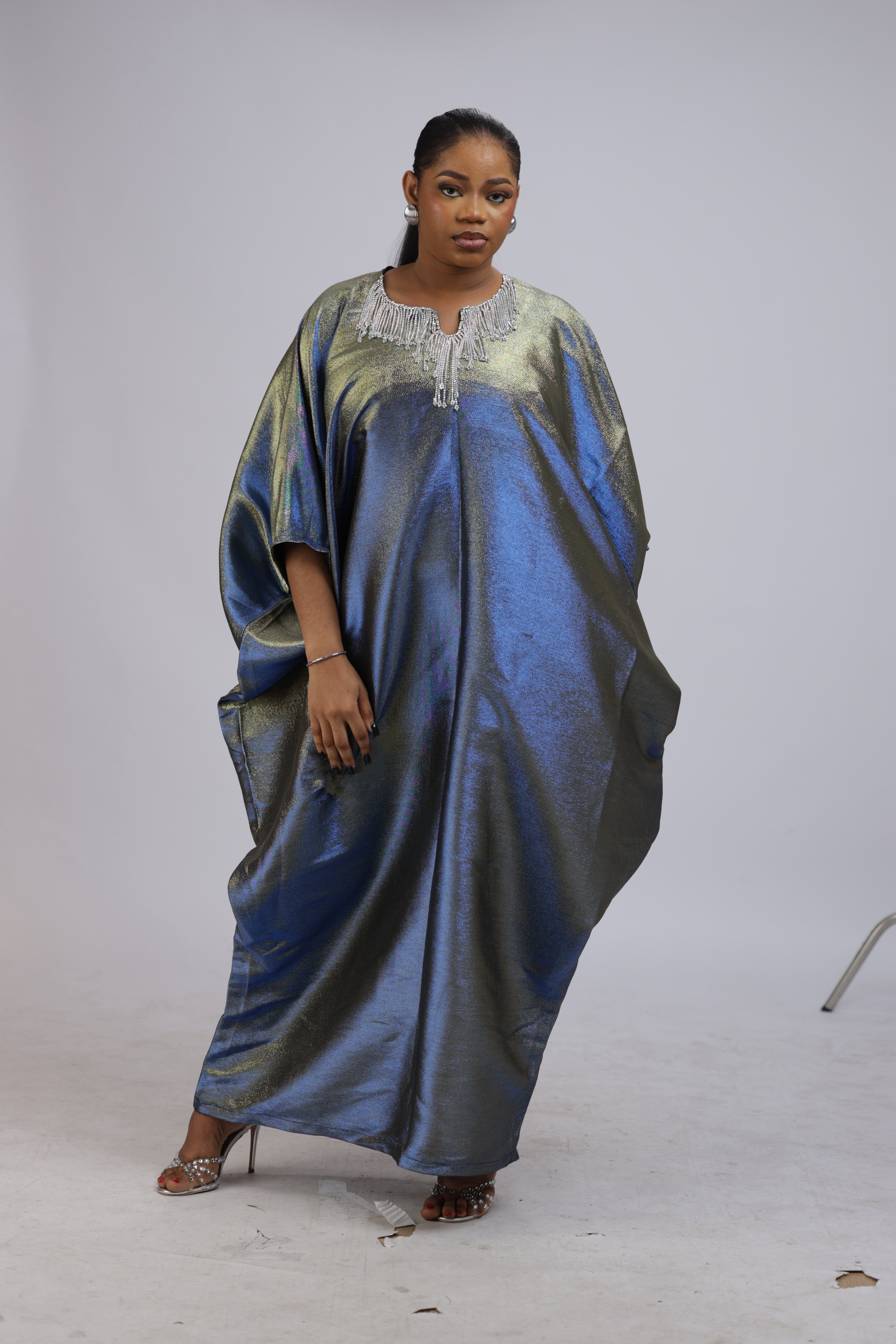 Woman wearing a shiny metallic blue-green cupped chain dress with loose sleeves and embellished neckline.
