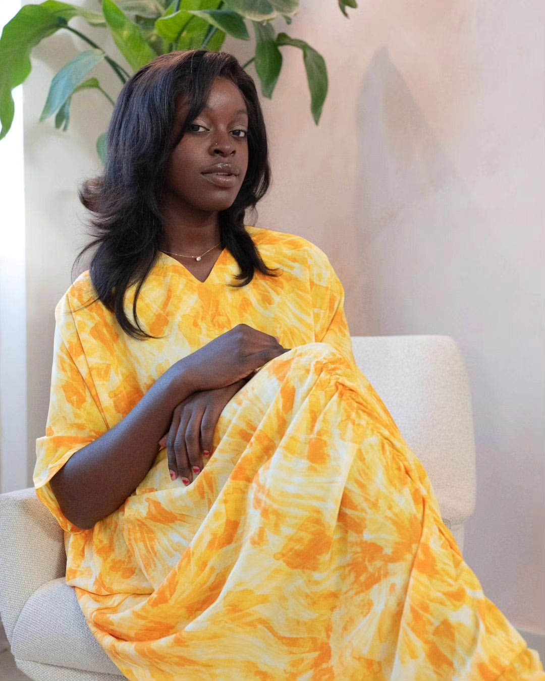 Woman wearing a yellow and orange tie-dye draped maxi dress with front gathers, standing indoors.
