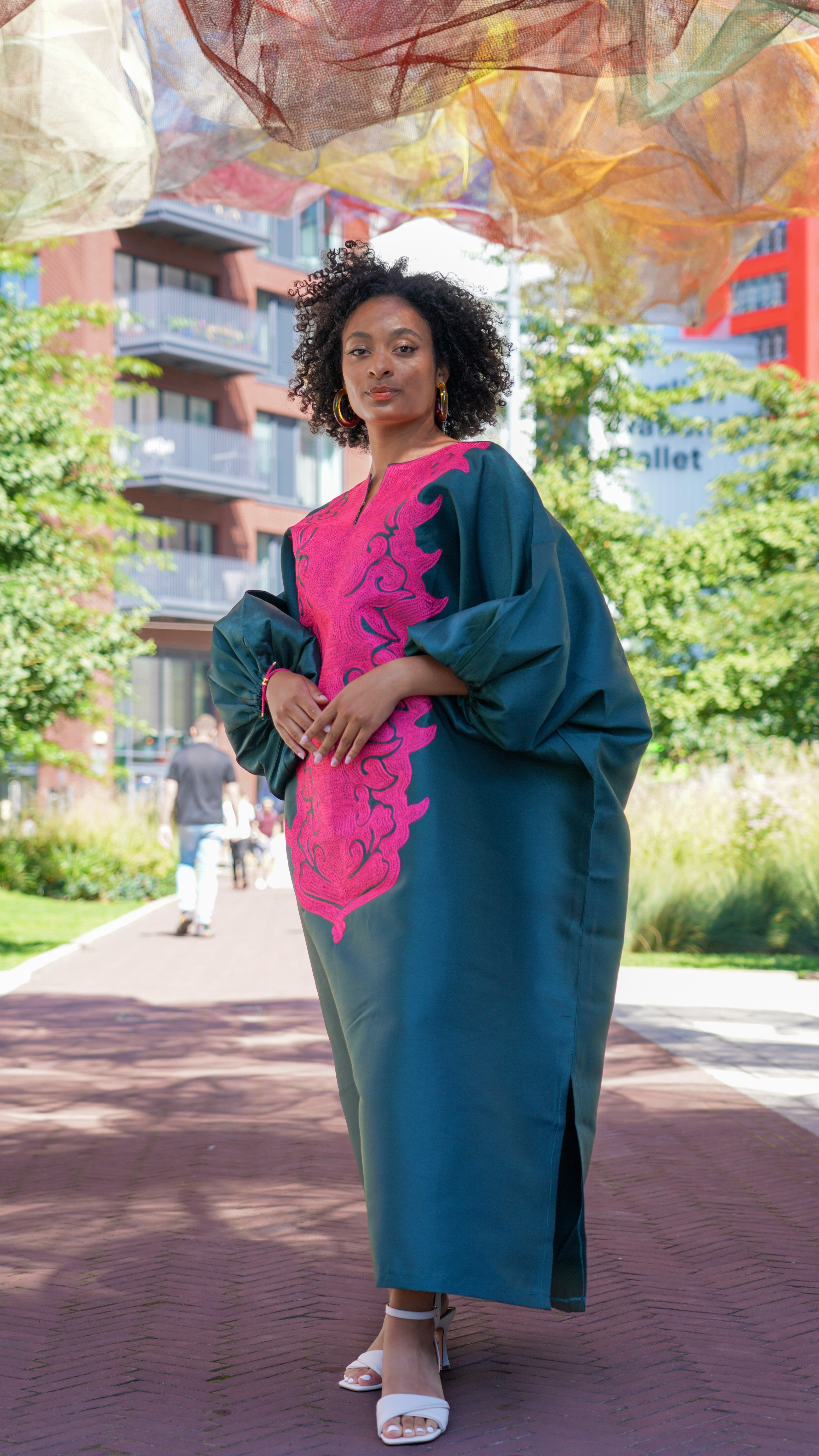 Model wearing luxurious teal Boubou dress with bold pink embroidery and voluminous sleeves.
