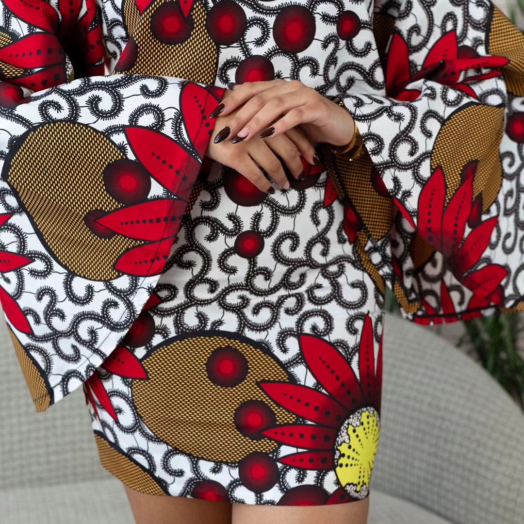 Woman wearing a bold Ankara two-piece set with flared sleeves and a fitted skirt in red, yellow, and black floral prints.
