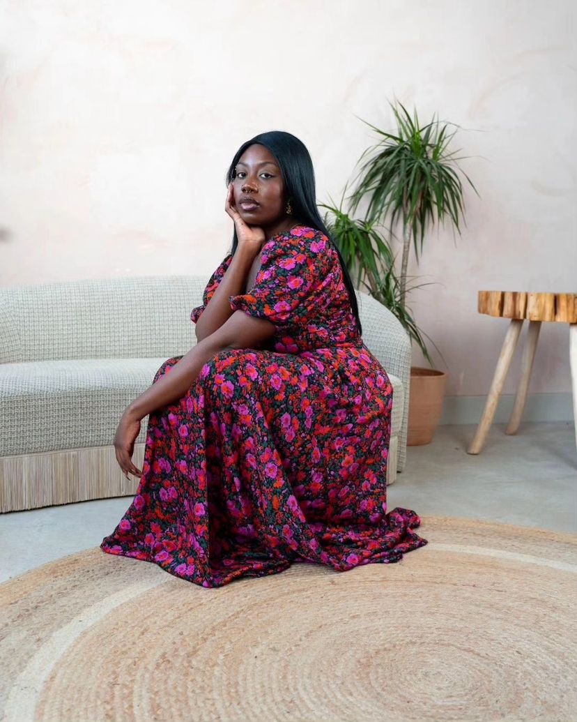 Woman wearing a long floral cut-out dress with puff sleeves in red and purple tones.
