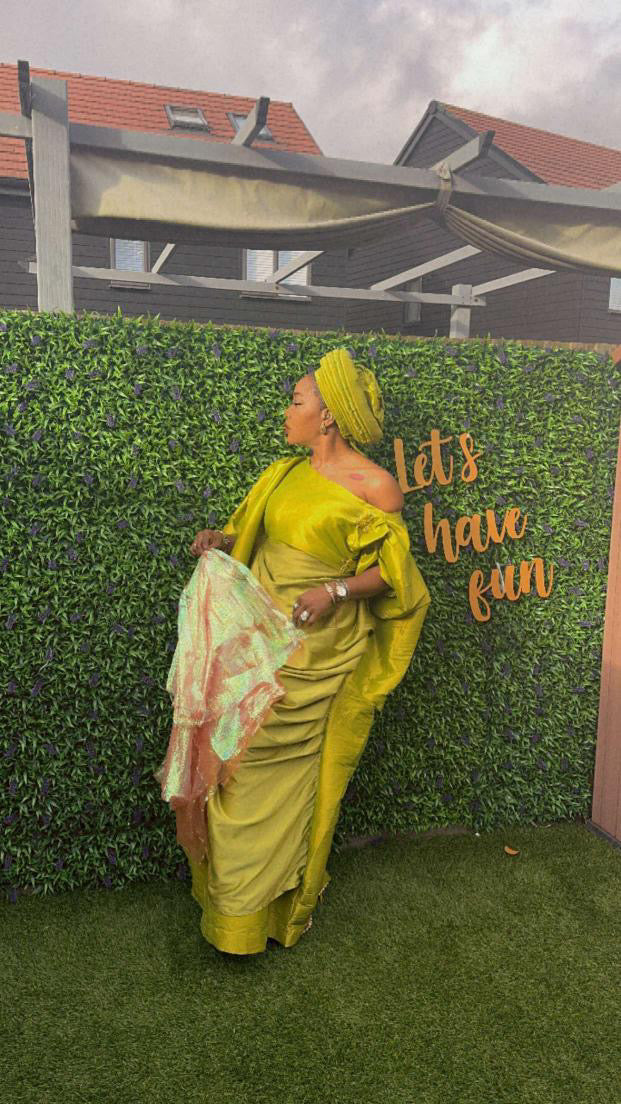 Elegant woman in a gold Show Stopper Boubou with draped detailing, posing gracefully at an outdoor event.
