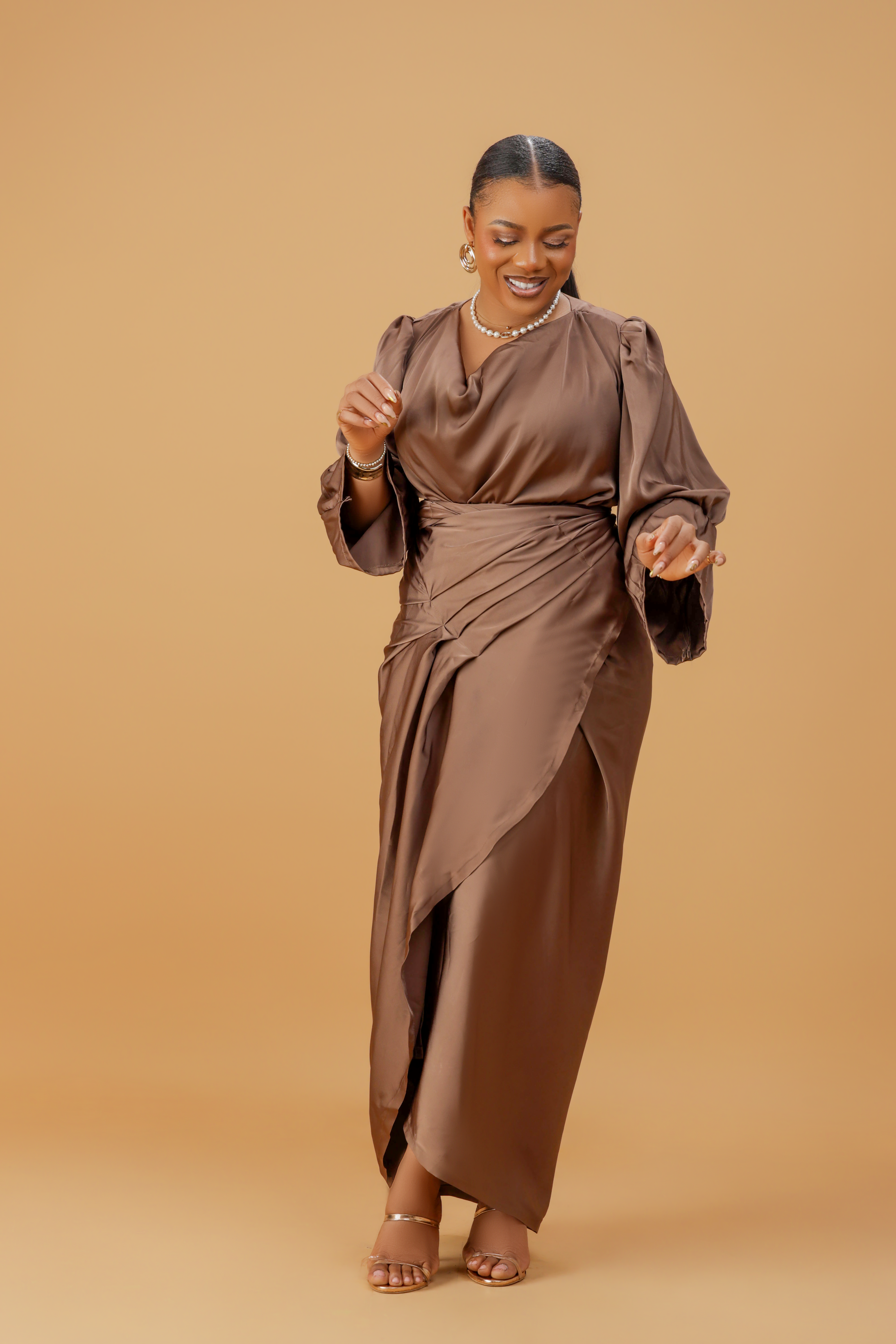 Woman wearing a coffee brown satin wrap gown with a cowl neckline and ruched waist, posing gracefully against a neutral background.
