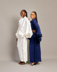 Two women wearing the Tella Dress: one in ivory, one in navy. Maxi gowns with ruffle sides, long sleeves, and bow-tie neckline.
