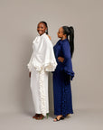 Two women wearing the Tella Dress: one in ivory, one in navy. Maxi gowns with ruffle sides, long sleeves, and bow-tie neckline.
