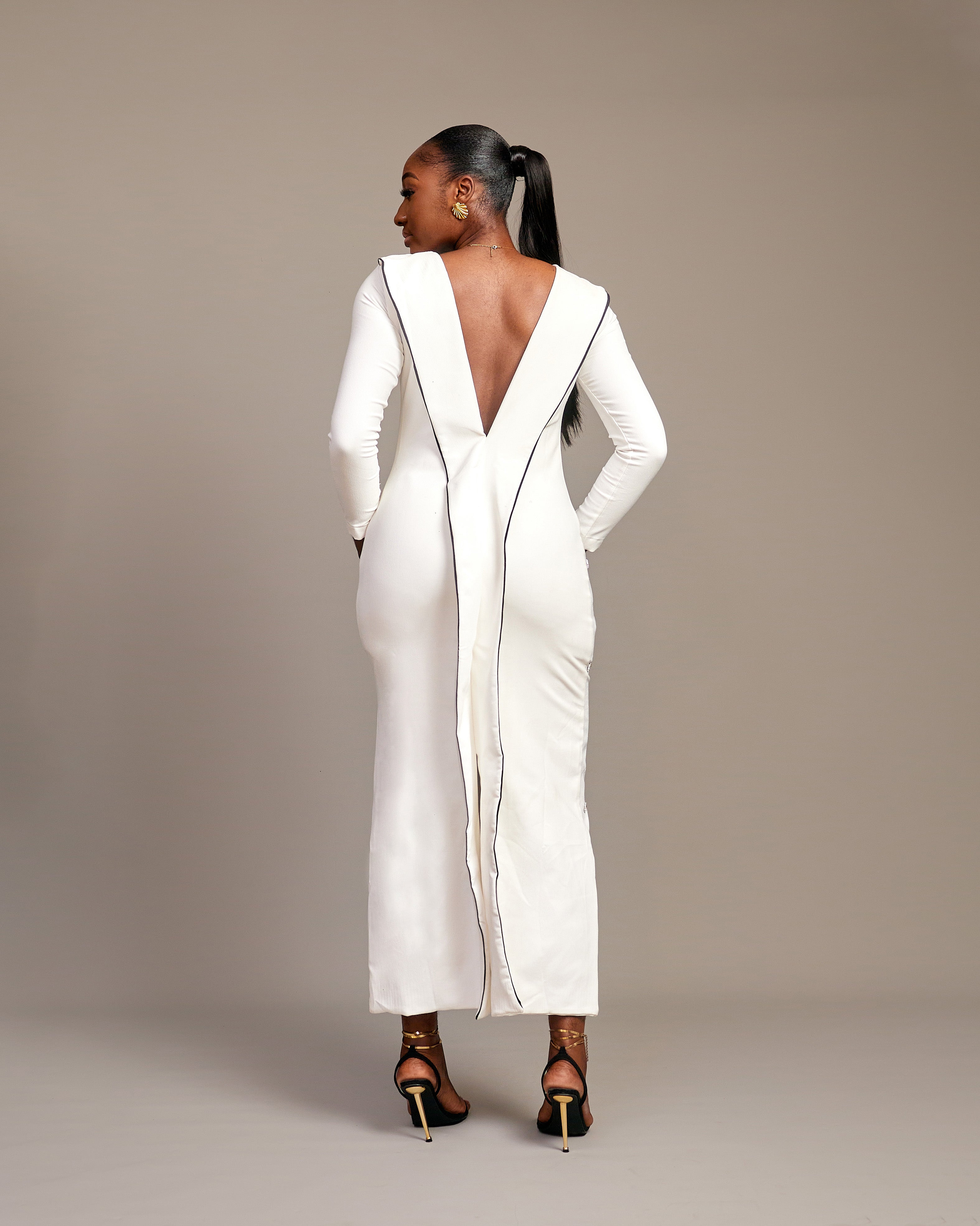 Woman wearing the Zola white maxi dress with bateau neckline, rhinestone embellishments, long sleeves, deep V-back plunge, and hemline slit.
