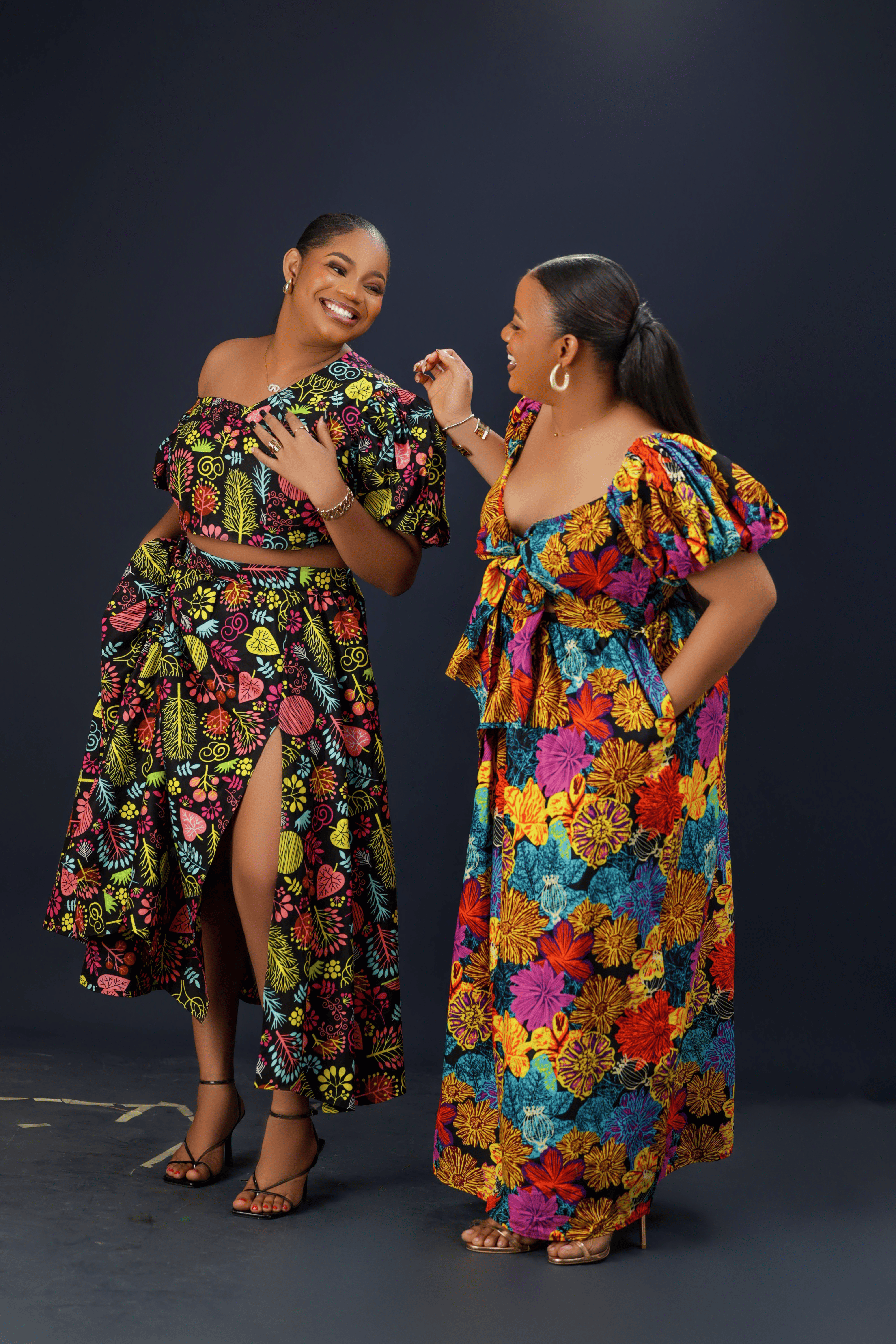  women wearing a vibrant floral maxi dress with puff sleeves, a front bow detail, and side pockets against a dark background.
