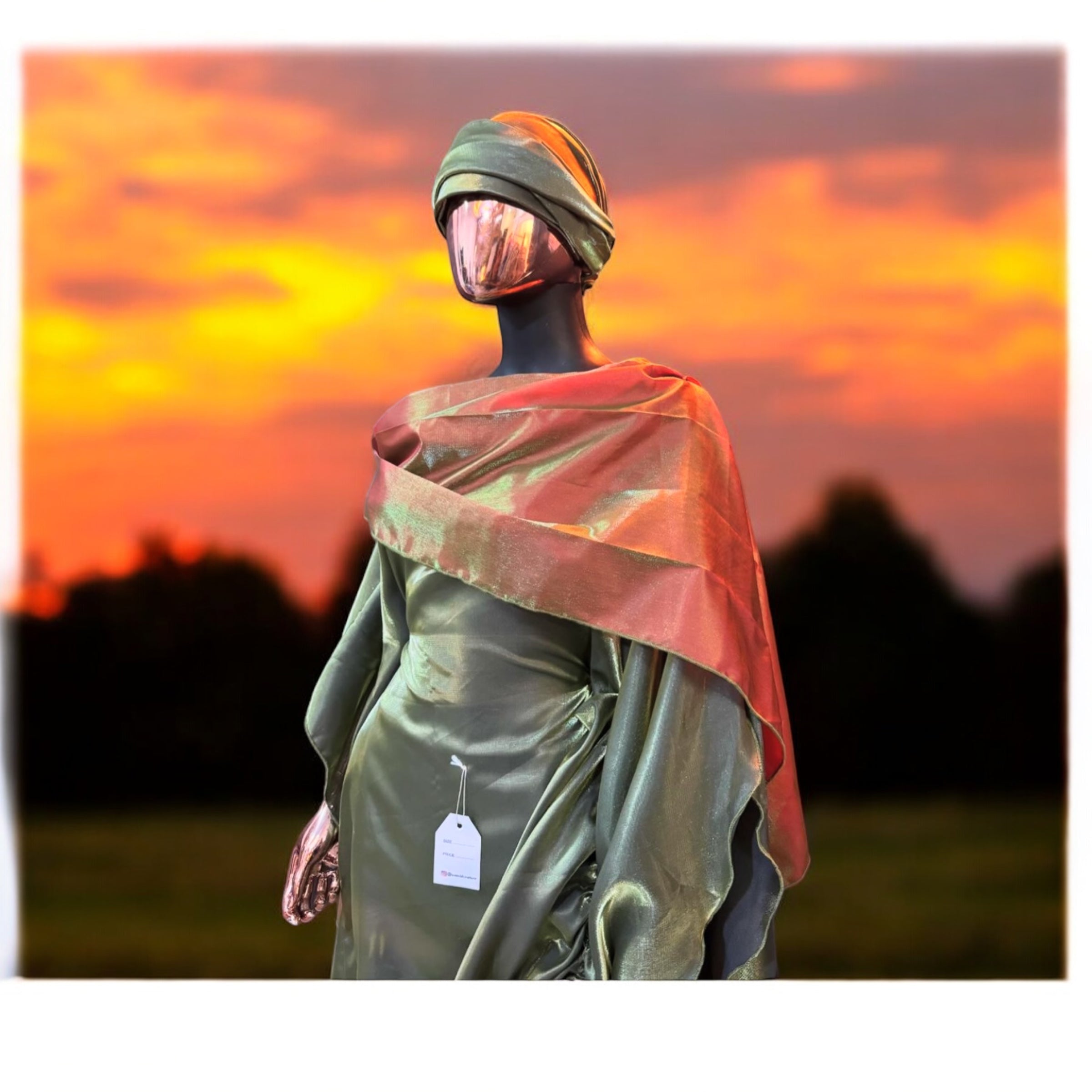 Olive green satin gown with ruched side draping, paired with a bronze-toned shawl and matching headwrap, displayed on a mannequin in an arched interior.
