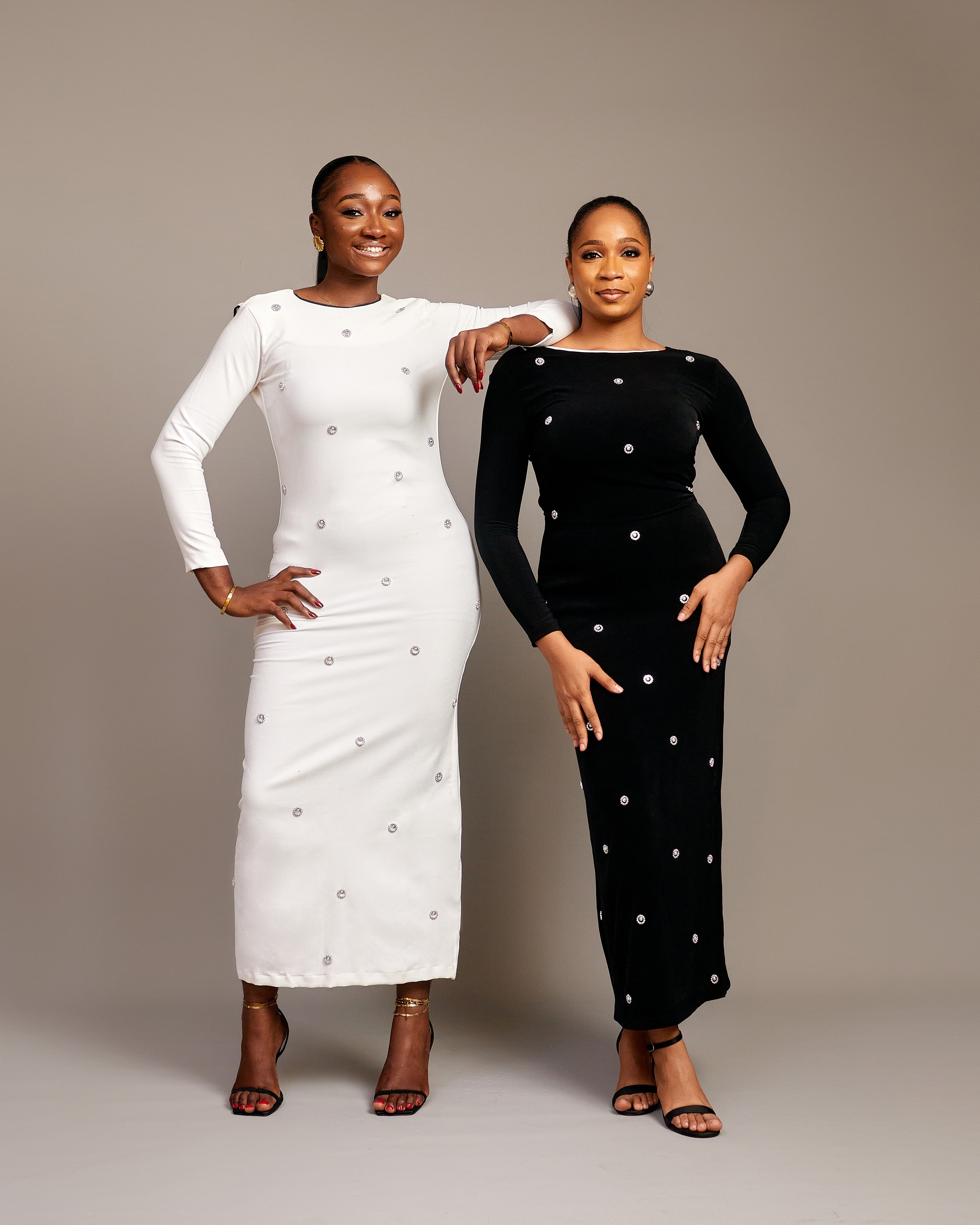 Women wearing the Zola maxi dress with bateau neckline, rhinestone embellishments, long sleeves, deep V-back plunge, and hemline slit.
