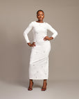 Woman wearing the Zola white maxi dress with bateau neckline, rhinestone embellishments, long sleeves, deep V-back plunge, and hemline slit.
