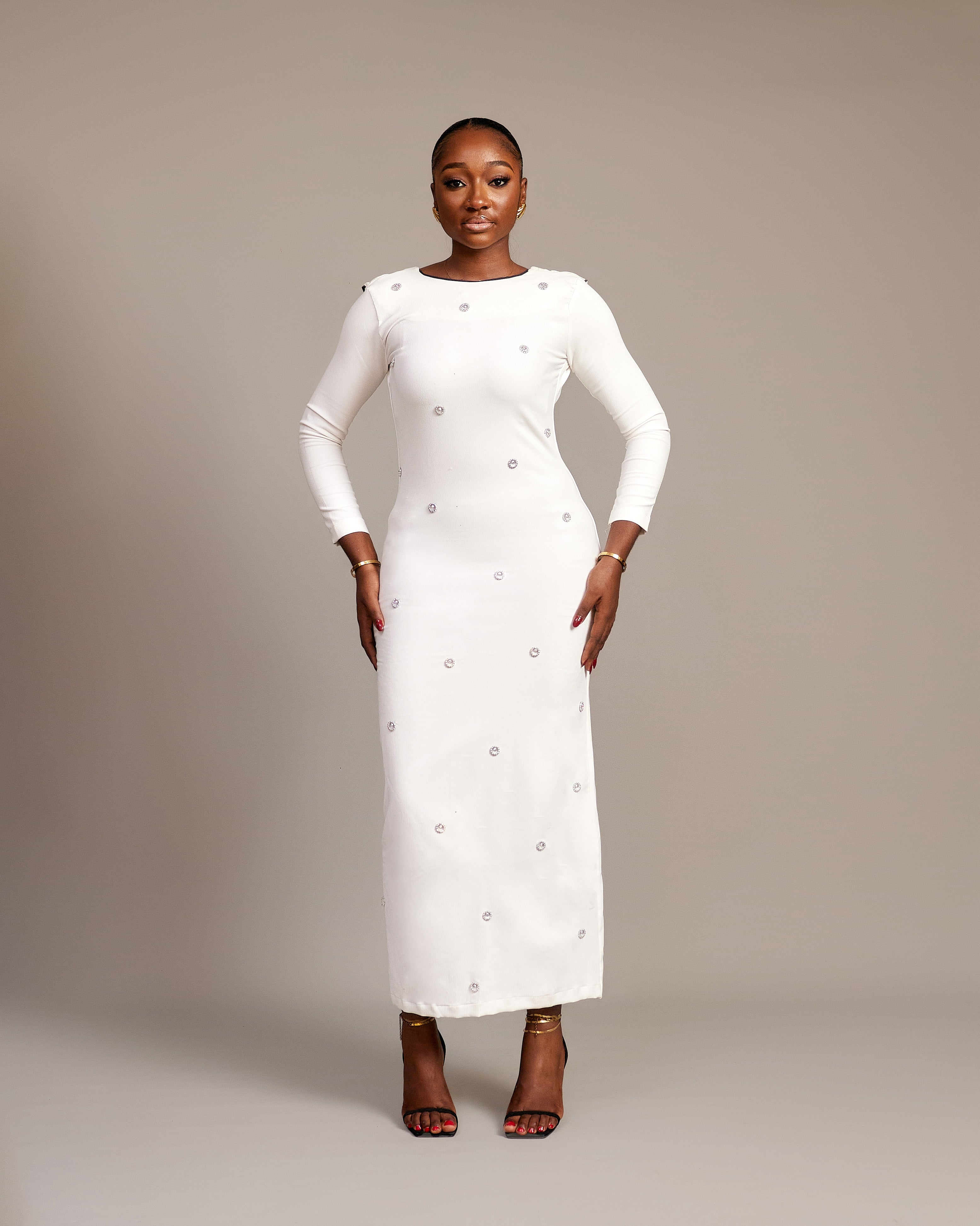 Woman wearing the Zola white maxi dress with bateau neckline, rhinestone embellishments, long sleeves, deep V-back plunge, and hemline slit.
