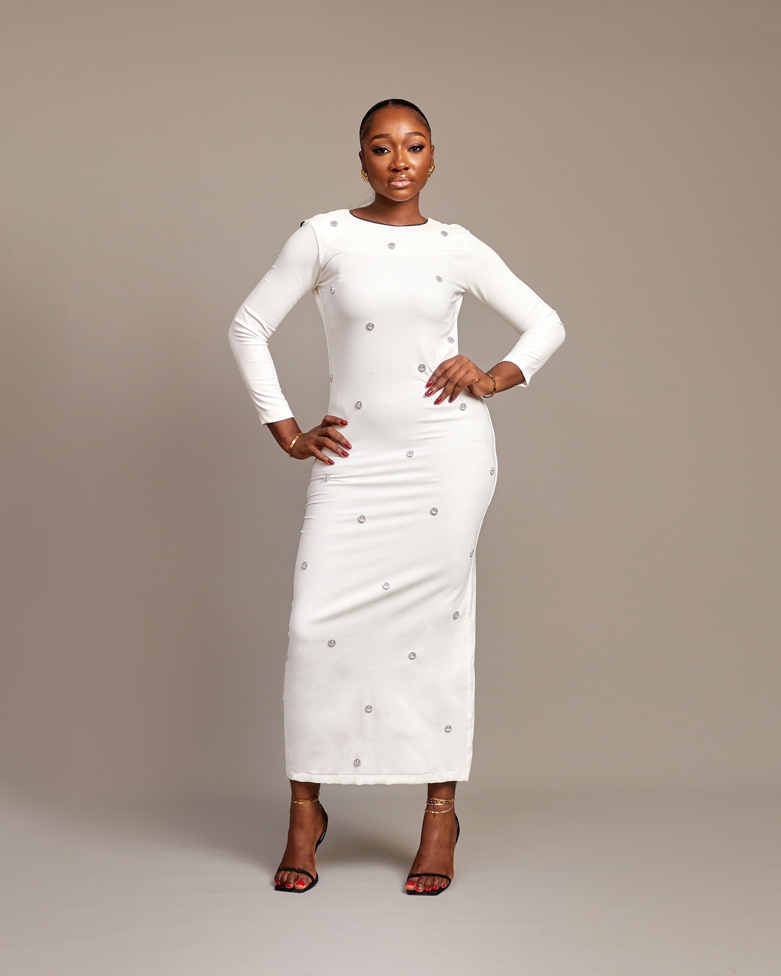 Woman wearing the Zola white maxi dress with bateau neckline, rhinestone embellishments, long sleeves, deep V-back plunge, and hemline slit.
