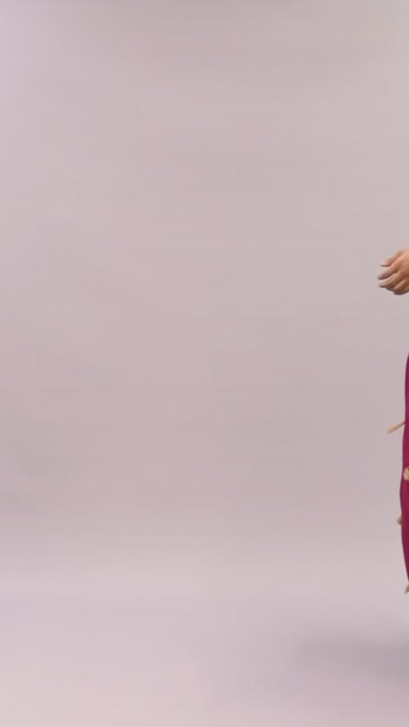 A lady wearing the Queen Ire two-piece set with textured ivory cape top and wine maxi skirt decorated with golden tassels, styled for weddings and cultural celebrations.
