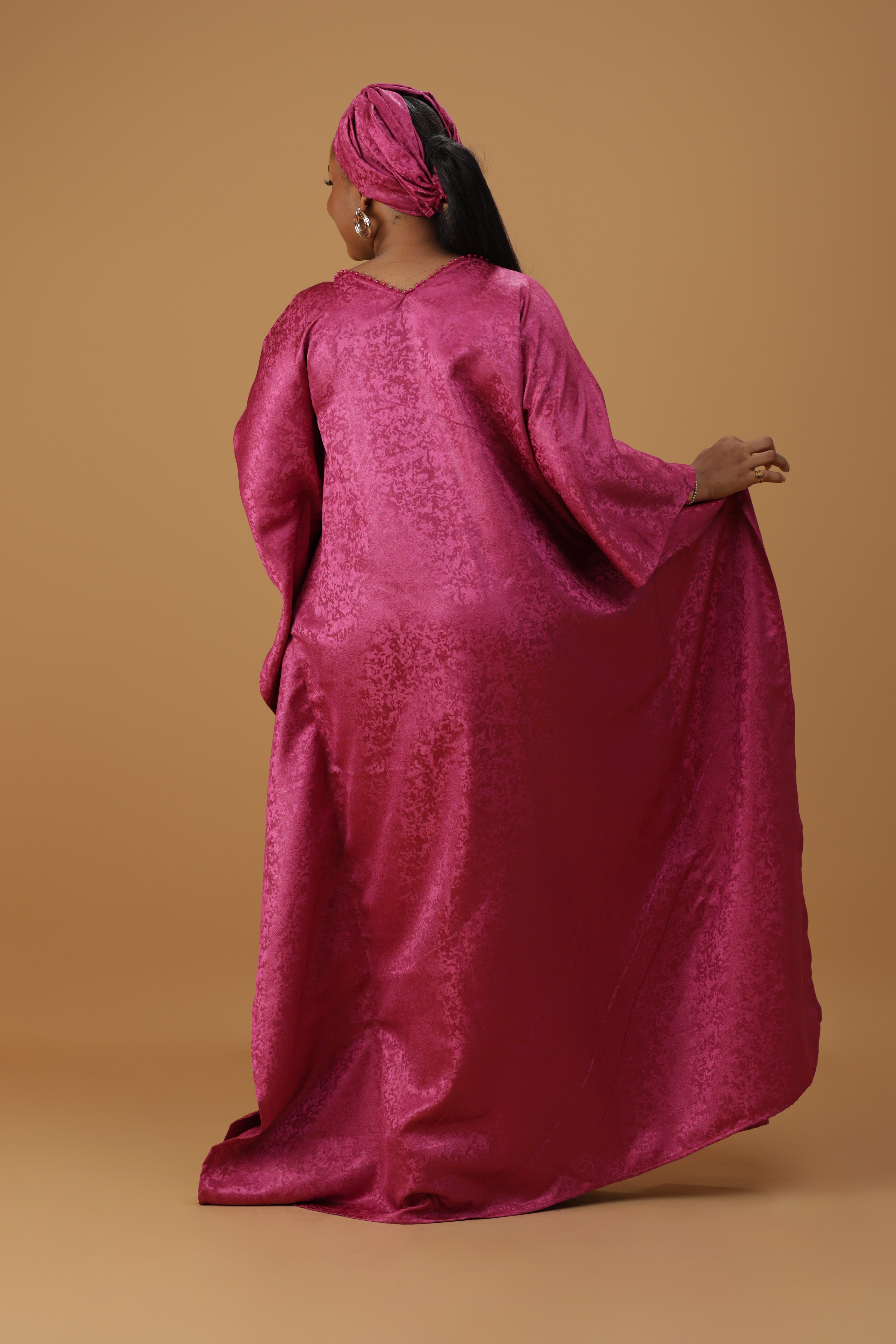 Woman wearing a radiant magenta kaftan with wide sleeves and a matching head wrap, styled for special occasions.
