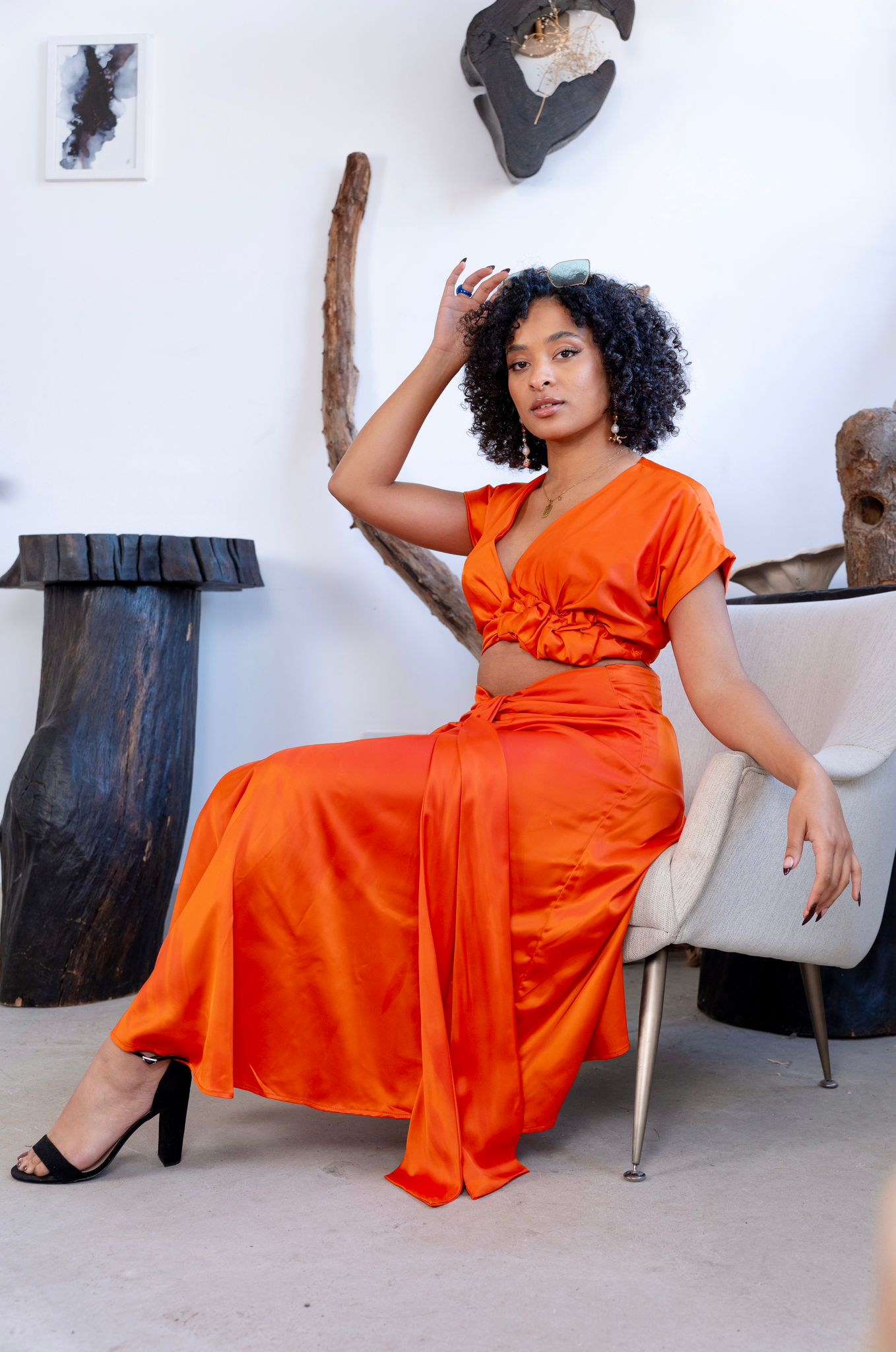  Woman wearing an orange satin crop top and matching ruched skirt, styled with statement glasses